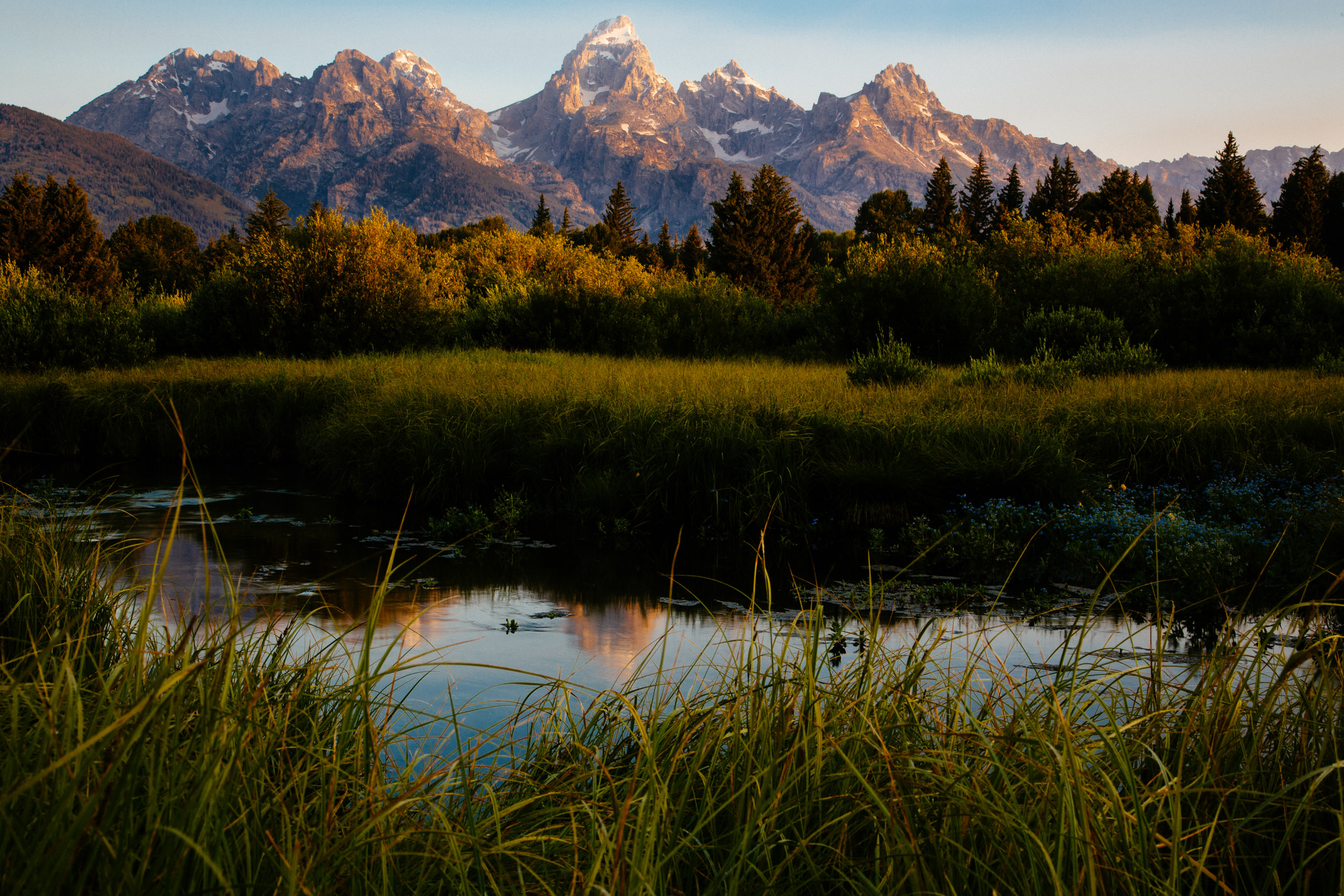 Iconic Grand Tetons at sunrise, reflected in a nearby creek