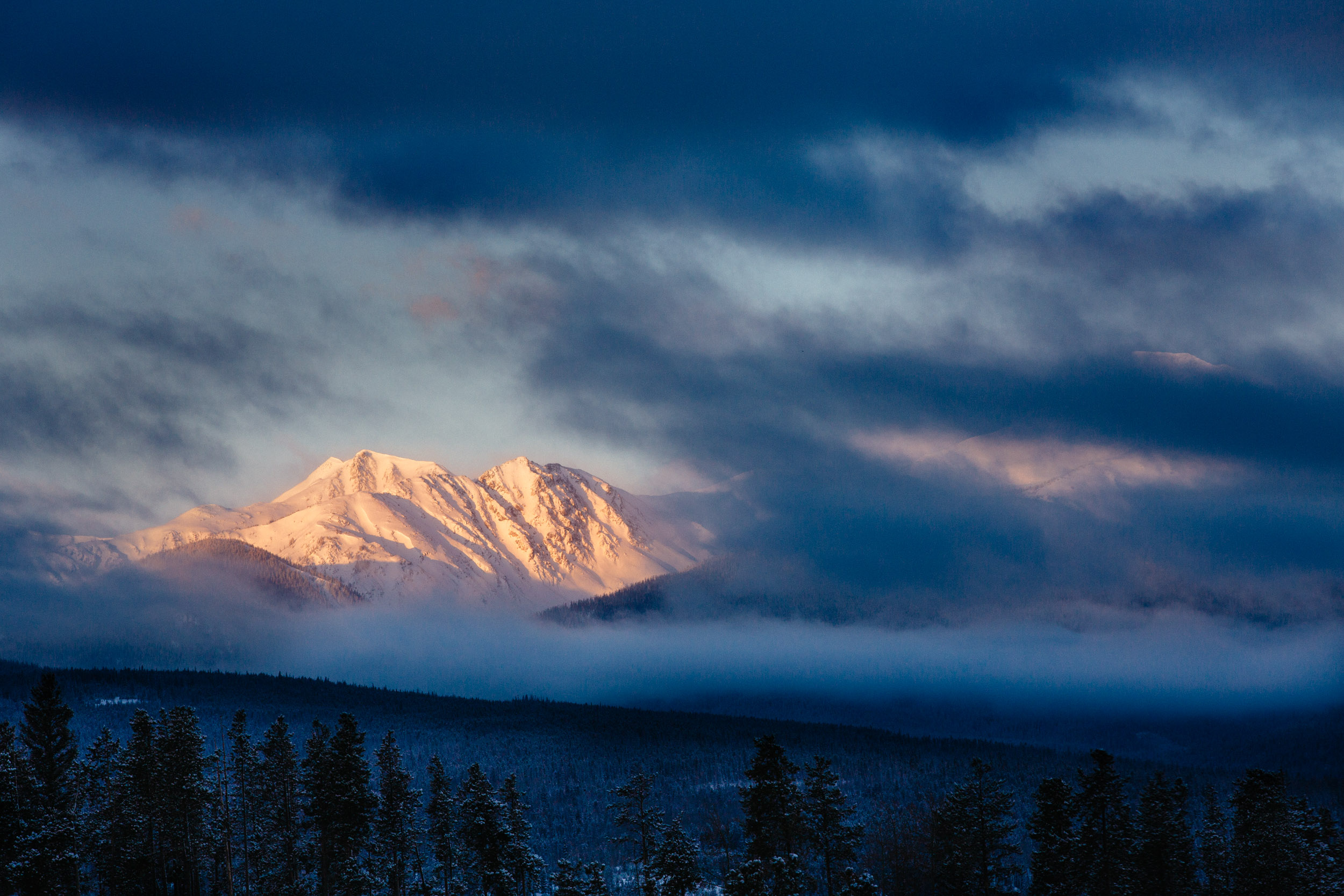 Byers peak at sunrise after a snowstorm, lit while area rocky mountains remain in the shade