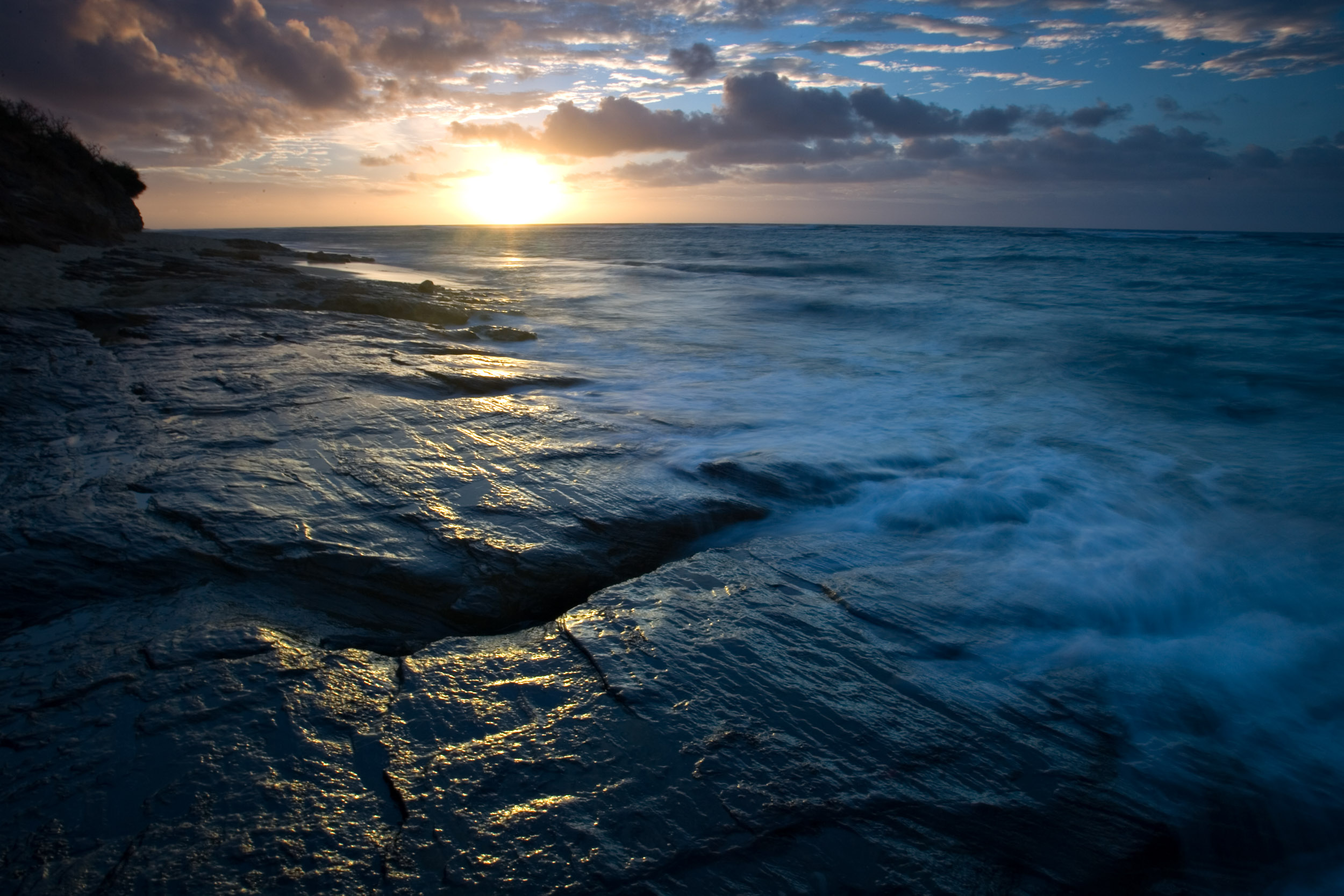 Gentle waves caress the aged rocks as the sun rises in Oahu