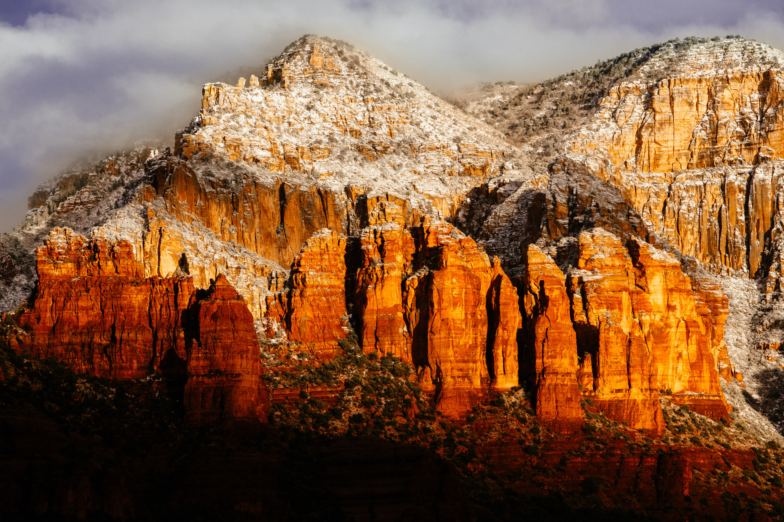 The sun peeks through parting clouds following a snowstorm, lighting up Sedona’s red rocks
